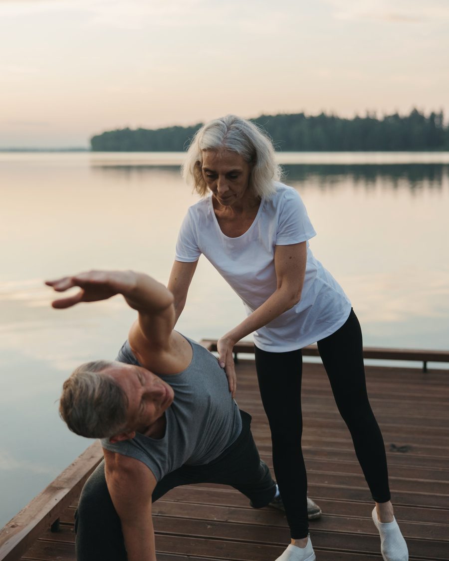 A woman helping a man exercise on a wooden pier